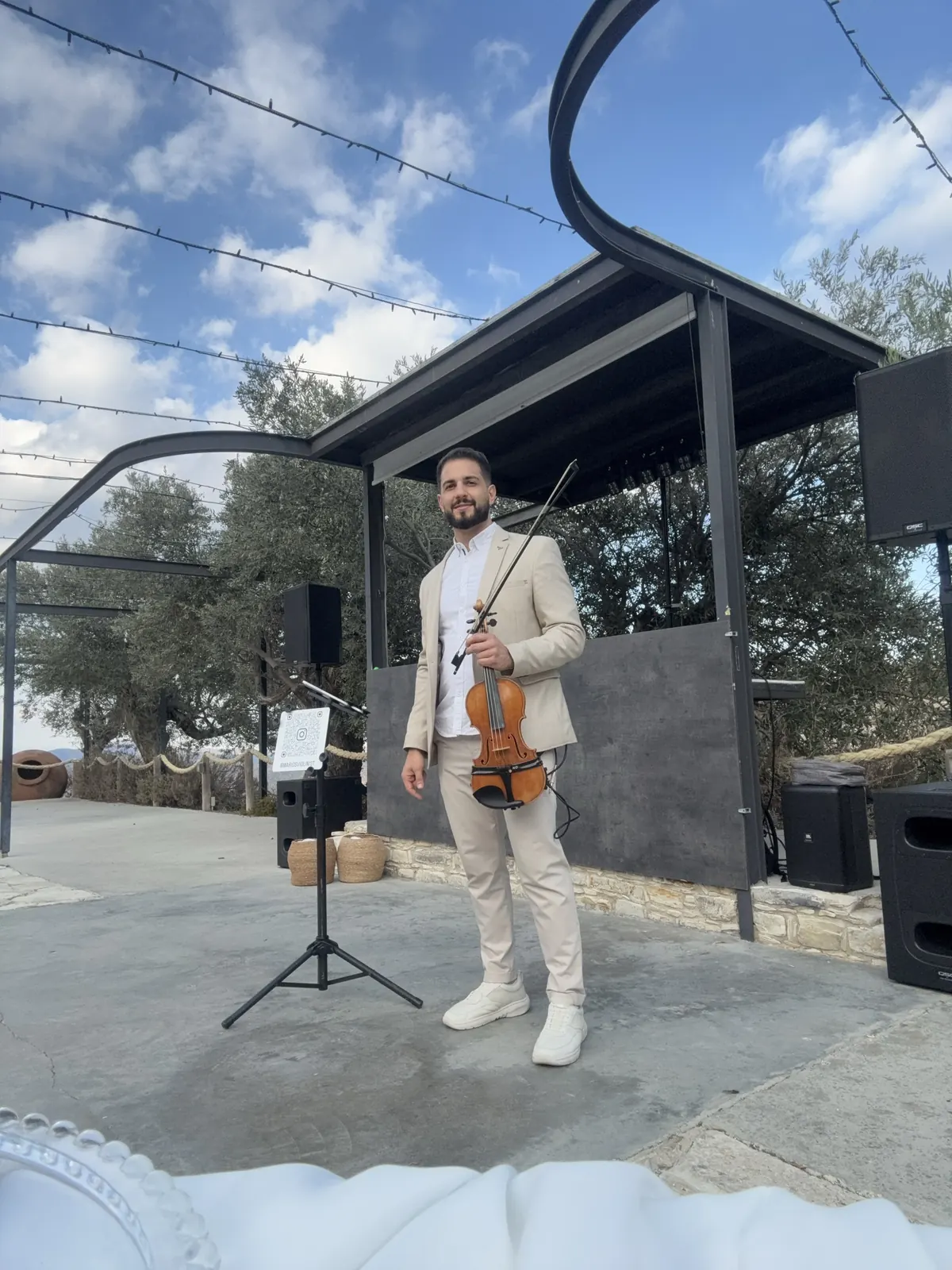 Marios in a beige suit holding his violin on an outdoor stage
