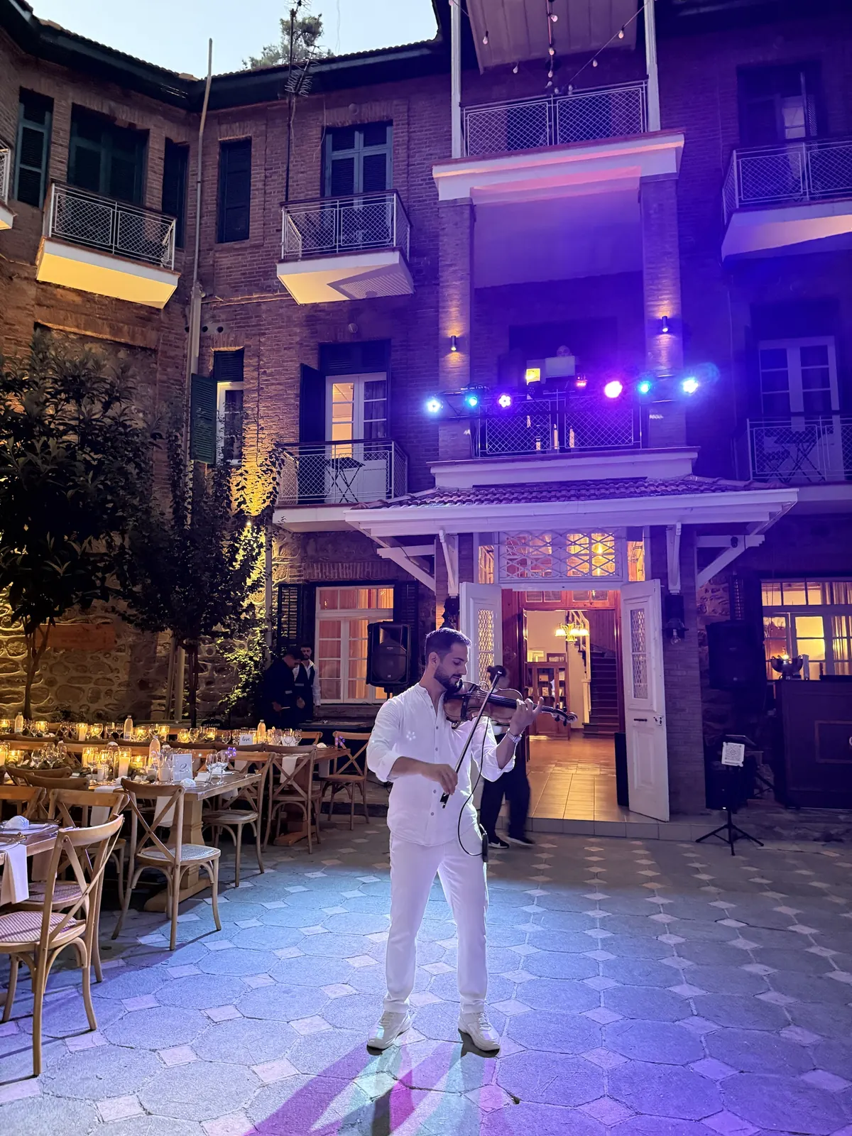 Marios playing violin in a courtyard at dusk with candlelit tables