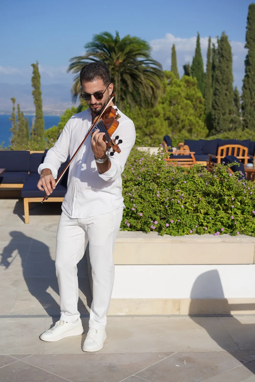 Marios playing violin in sunglasses on a terrace above the sea