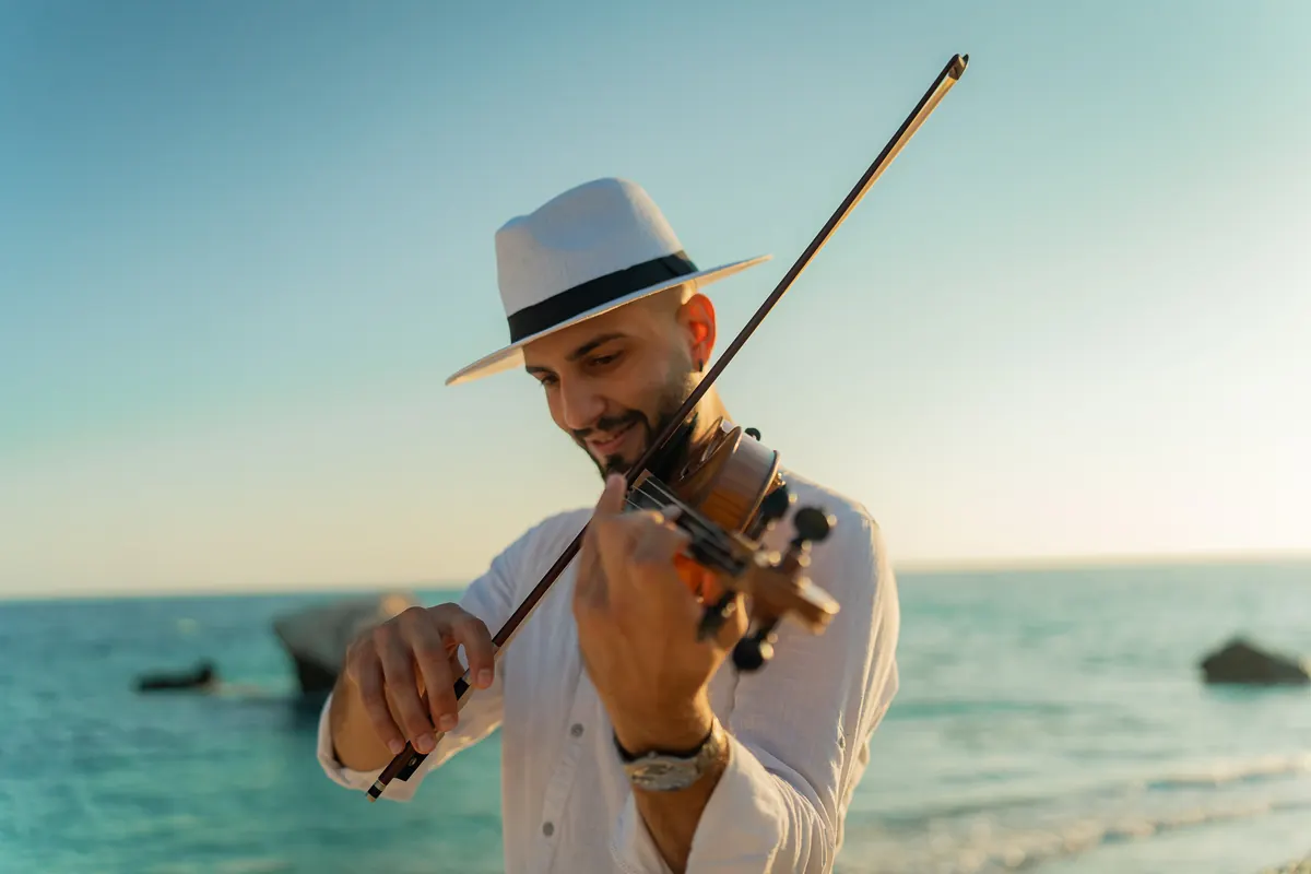 Marios in a white hat playing violin by the sea