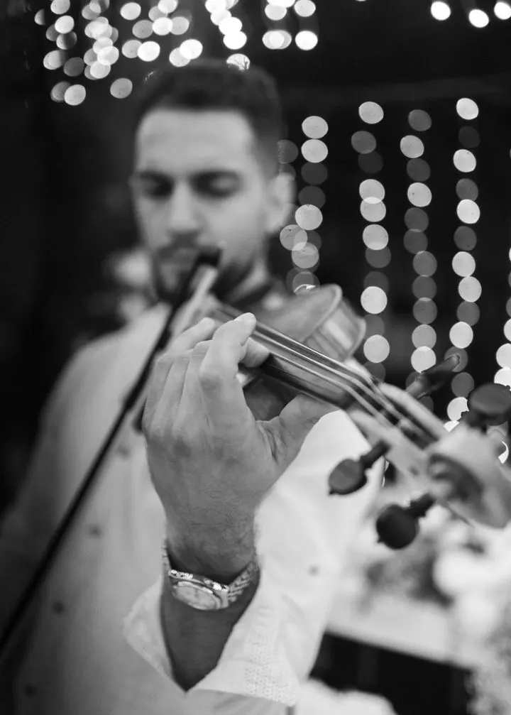 Black and white close-up of Marios’s hand on the violin with bokeh lights