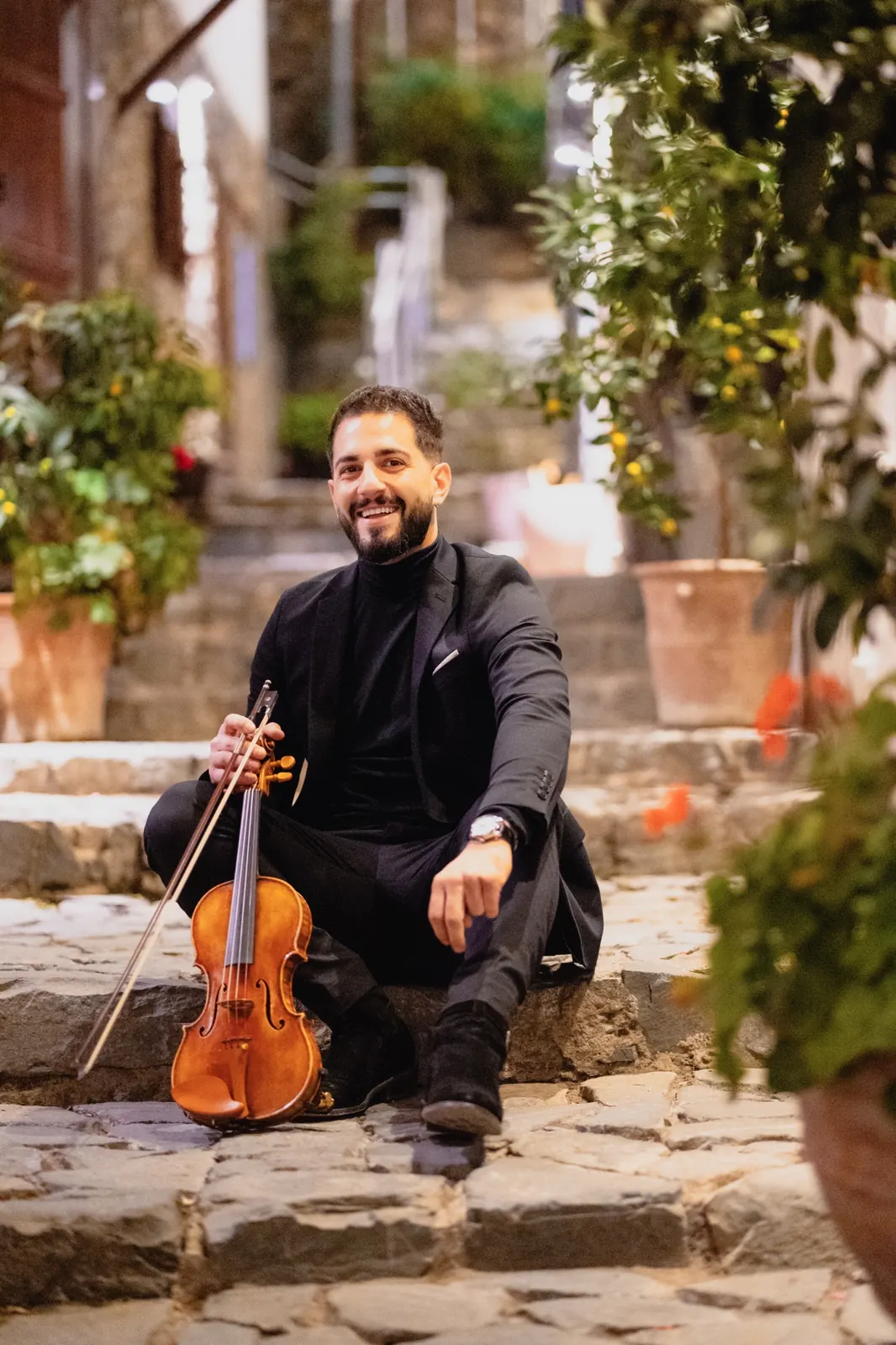 Marios sitting on stone steps with his violin, smiling
